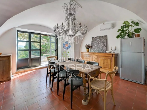 Intérieur d'une maison avec une table en bois, des chaises, et une grande fenêtre donnant sur un paysage.