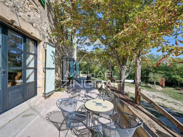 Terrasse d'une propriété en pierre avec table et chaises, entourée de verdure.