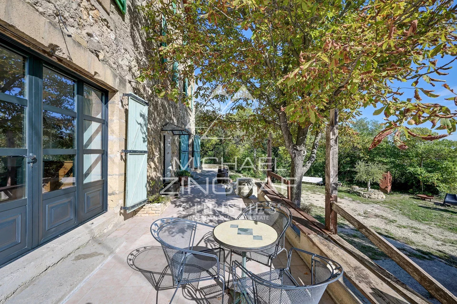 Terrasse d'une propriété en pierre avec table et chaises, entourée de verdure.