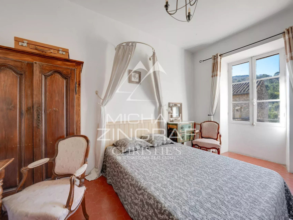 Chambre d'une demeure du XIXe siècle avec lit, chaise et armoire en bois, fenêtres donnant sur l'extérieur.