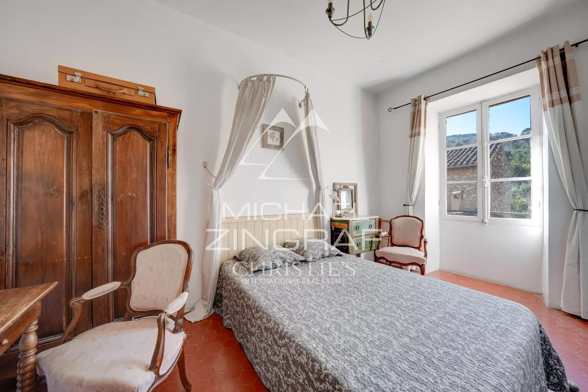 Chambre d'une demeure du XIXe siècle avec lit, chaise et armoire en bois, fenêtres donnant sur l'extérieur.