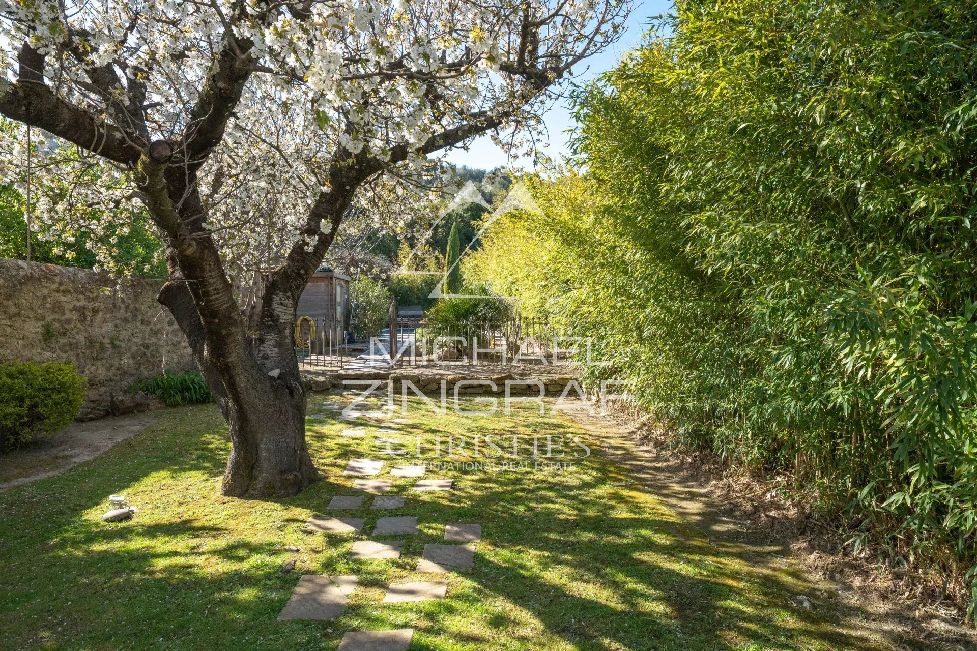 Jardin d'une demeure provençale avec un arbre en fleurs et des haies.