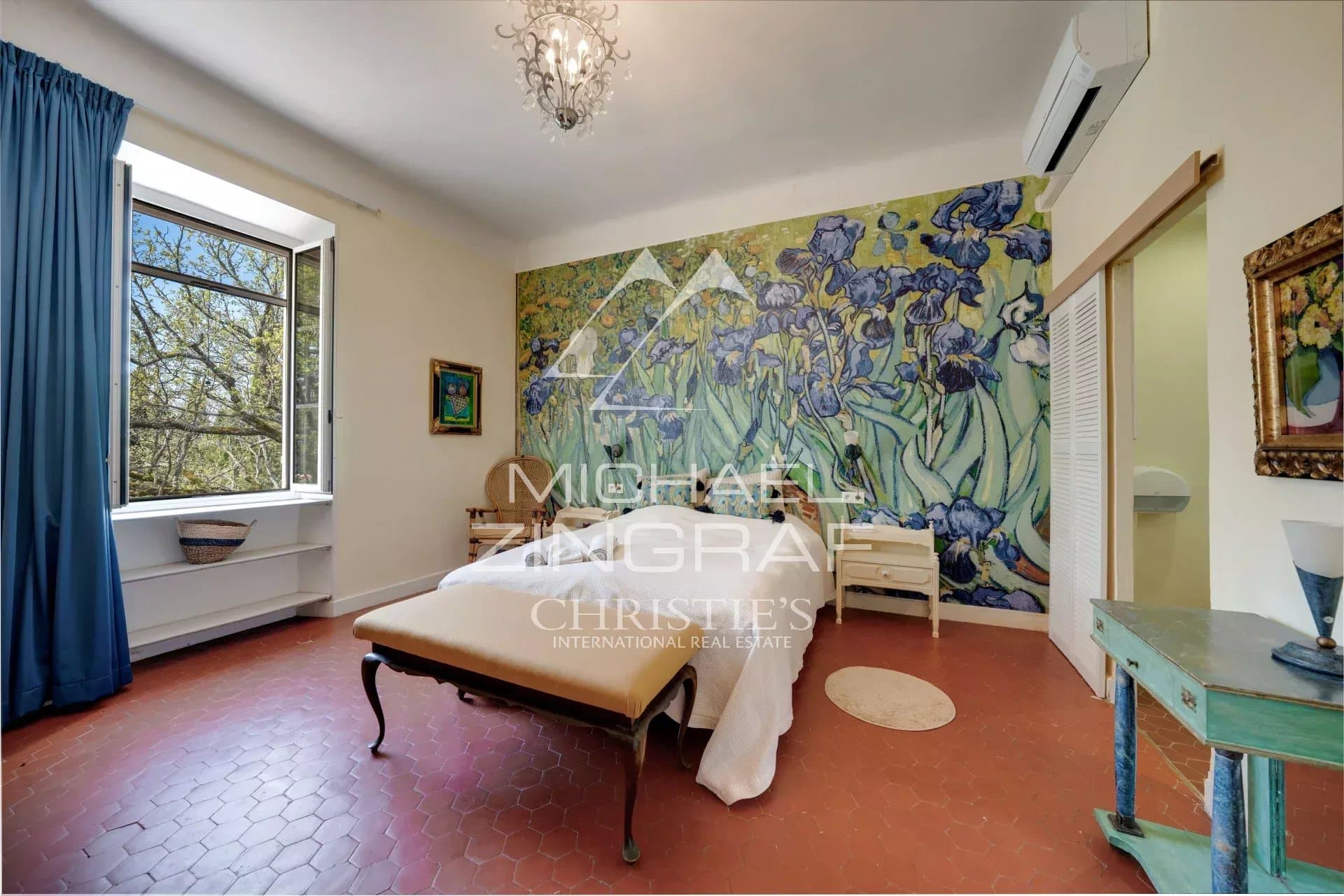 Room in a Provençal estate with a large wall decorated with flowers, windows open onto nature.