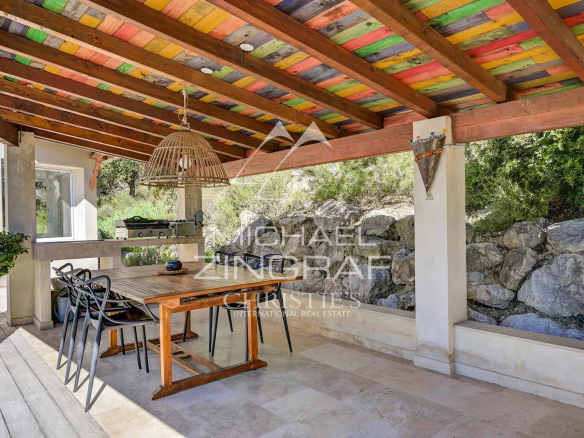 Wooden terrace with table and chairs under a colorful awning, surrounded by greenery.