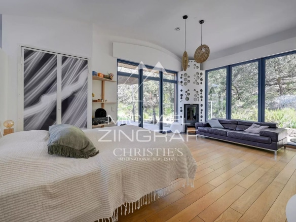 Interior of a bright house with a living room and a bedroom, large windows overlooking nature.