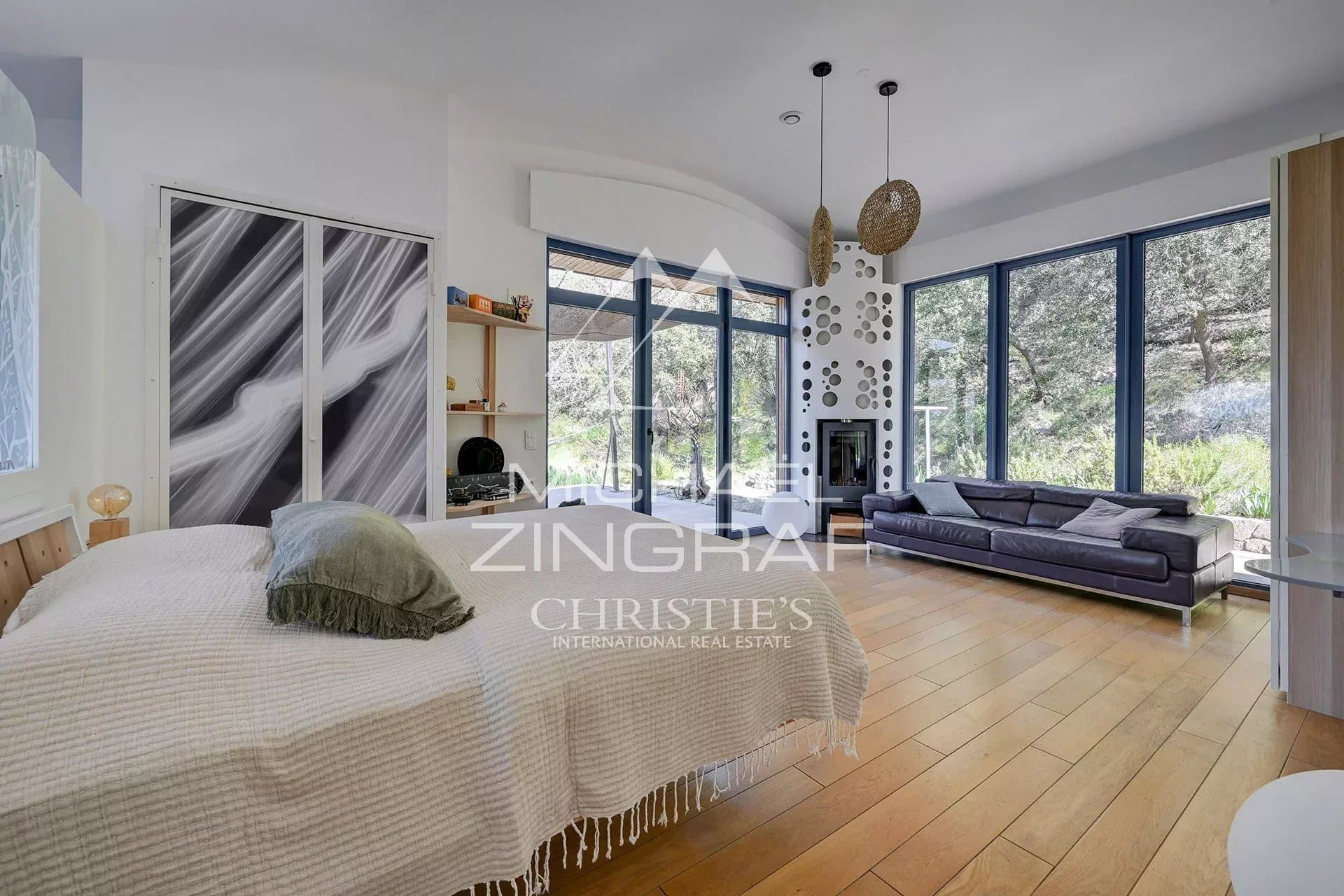 Interior of a bright house with a living room and a bedroom, large windows overlooking nature.