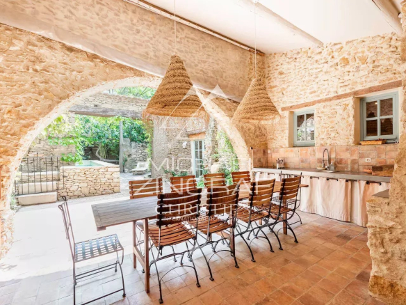 Intérieur d'une magnanerie rénovée avec une grande table en bois et des chaises en fer, murs en pierre apparente.