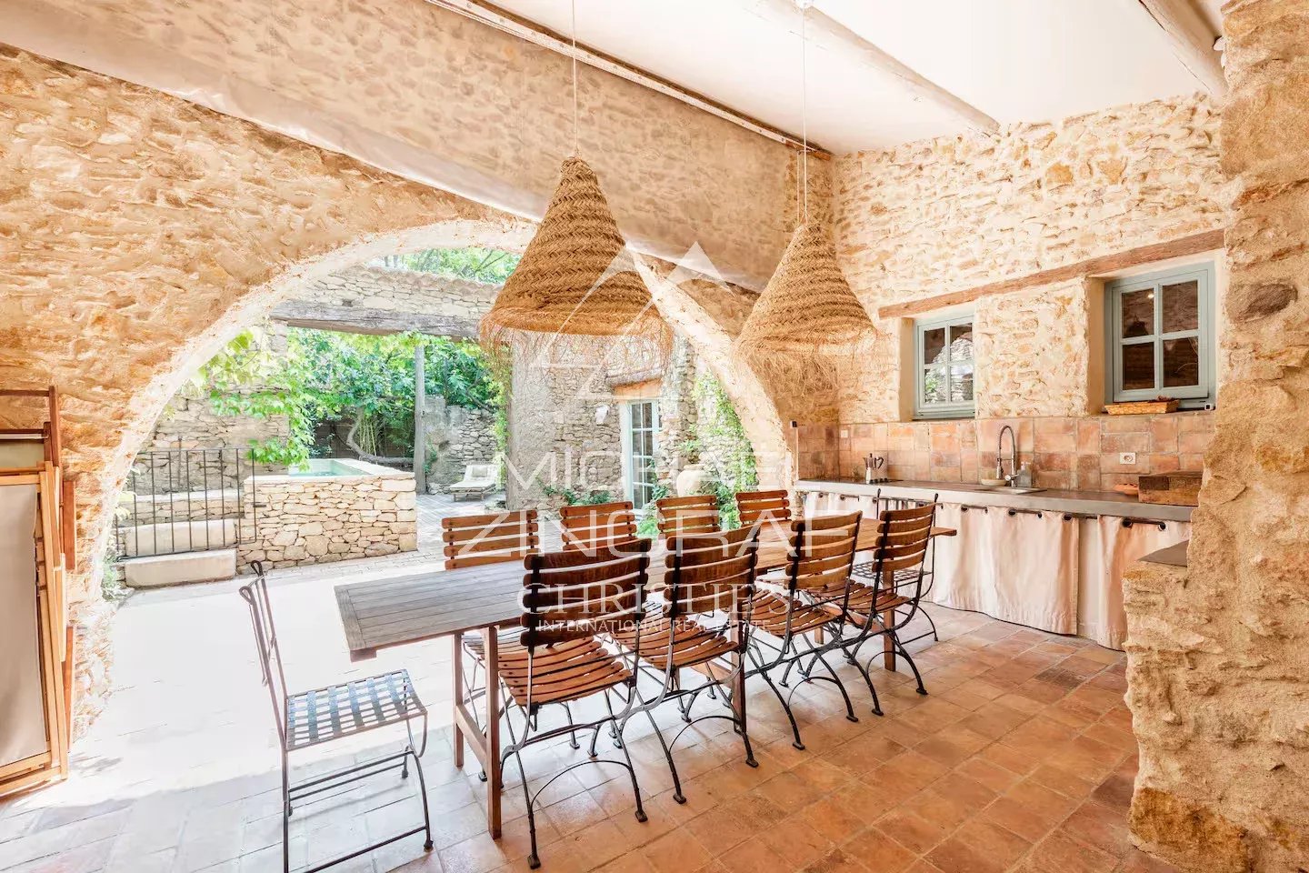 Intérieur de la Magnanerie du XVIIIe Intérieur d'une magnanerie rénovée avec une grande table en bois et des chaises en fer, murs en pierre apparente.