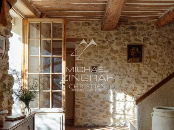 Intérieur lumineux d'une magnanerie rénovée avec des murs en pierre et des poutres en bois.