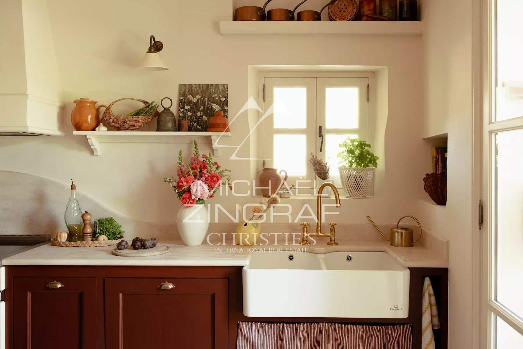 Cuisine rénovée d’une magnanerie Cuisine moderne avec évier en céramique et décor provençal, éléments en bois et plantes.