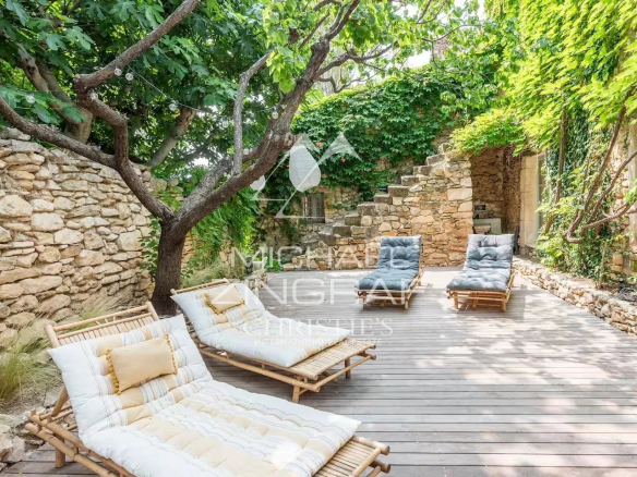 Wooden terrace with sun loungers surrounded by greenery and stone walls.