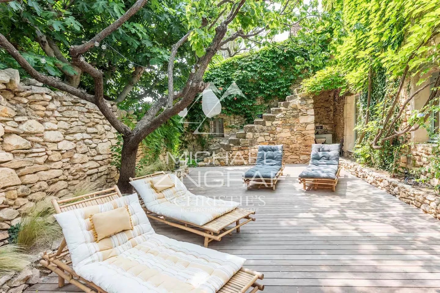 Terrasse de la magnanerie rénovée Terrasse en bois avec chaises longues entourée de verdure et de murs en pierre.