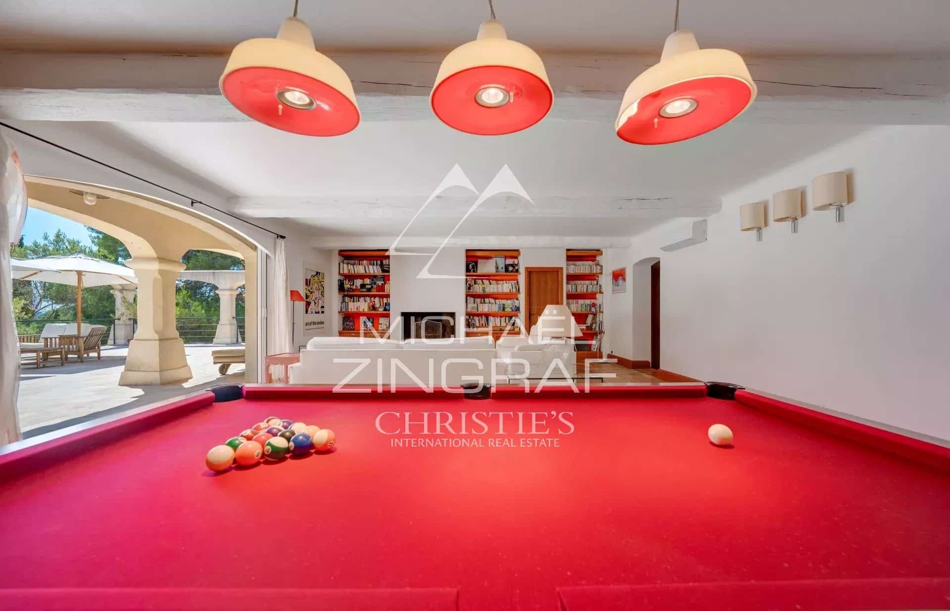 Table de billard dans une salle lumineuse avec accès à l'extérieur, décorée de livres et de lampes.