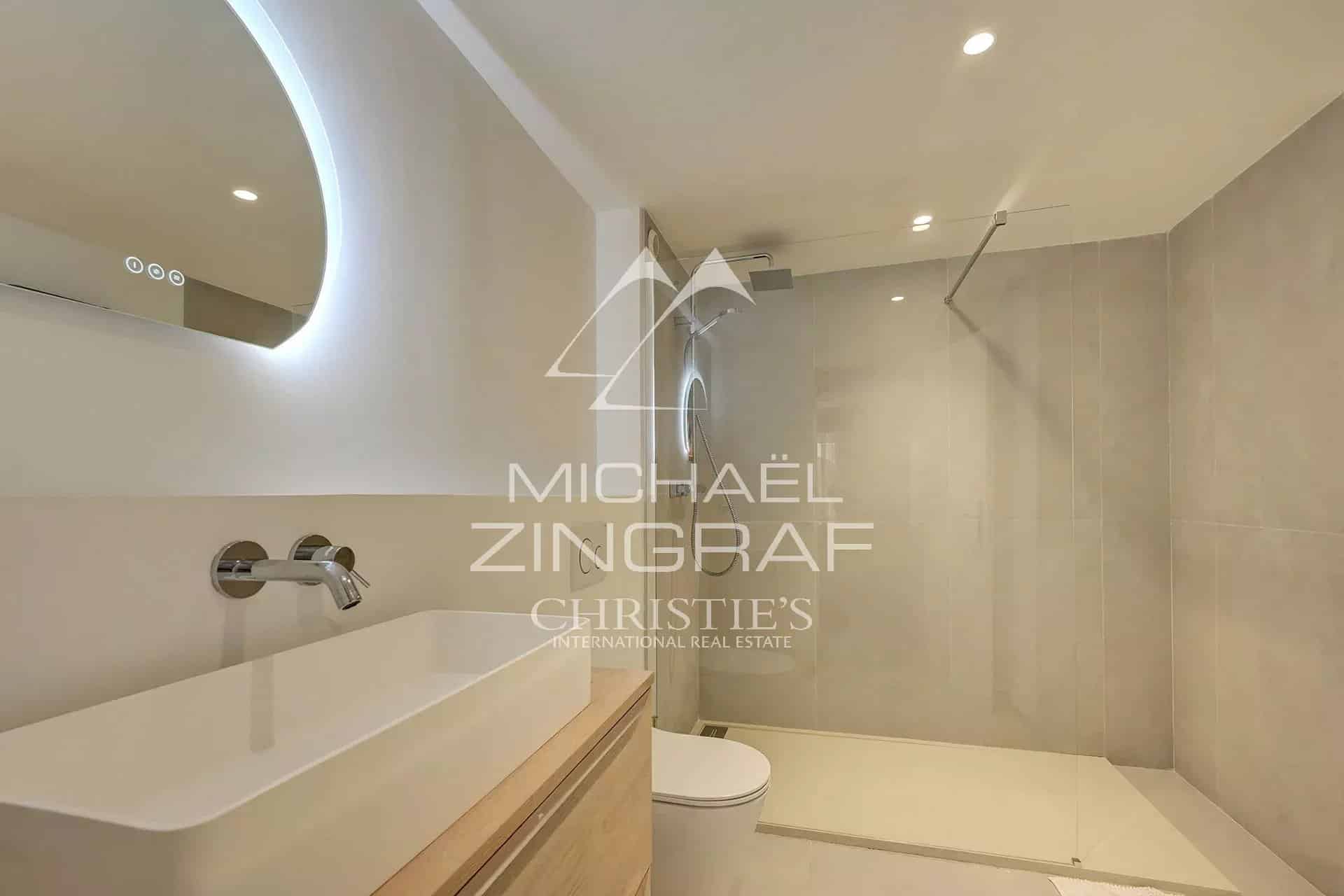 Modern bathroom with shower and sink, light walls and integrated lighting.