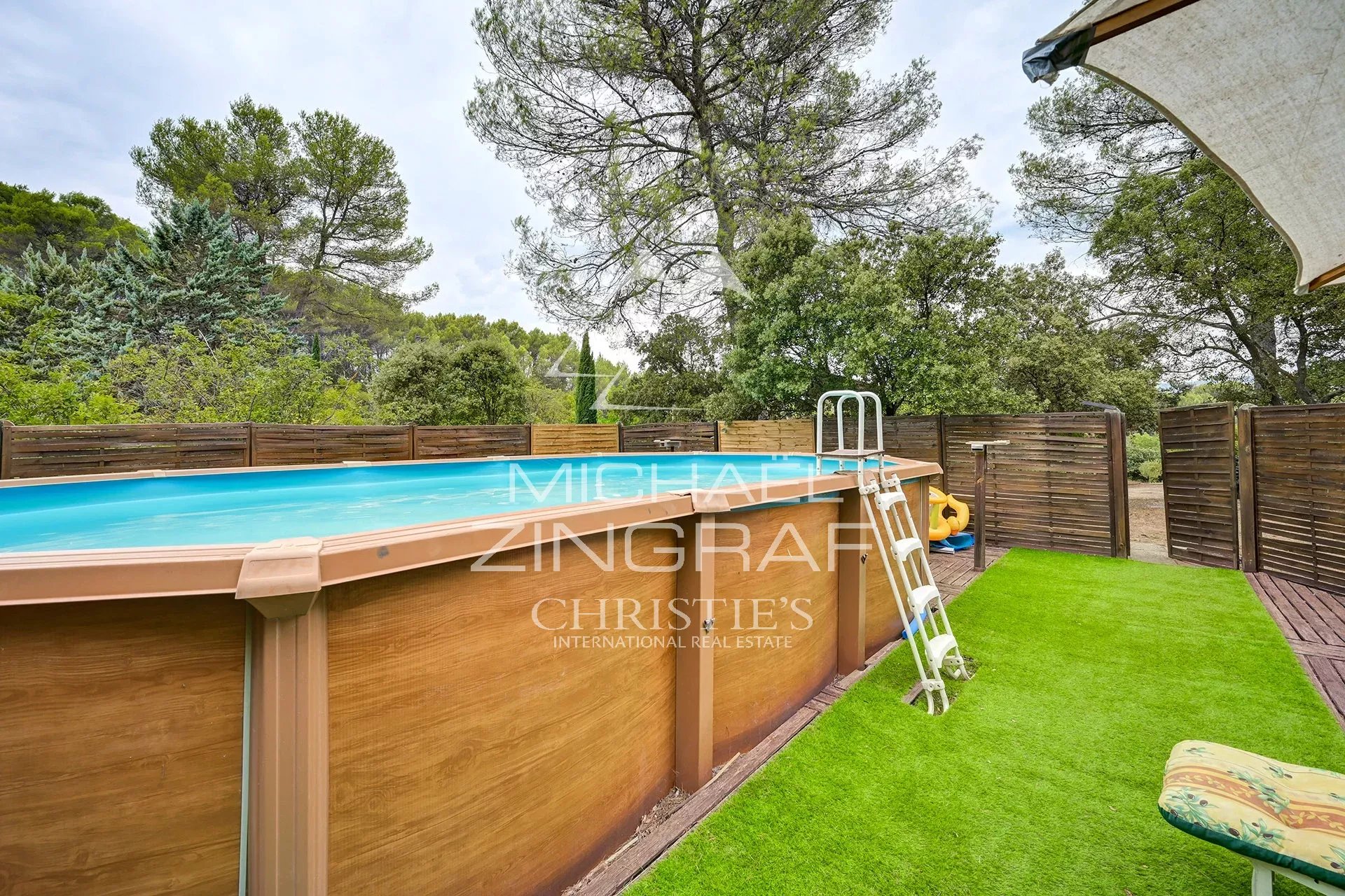 Above-ground swimming pool surrounded by wooden terraces and greenery in a family home in Fuveau.