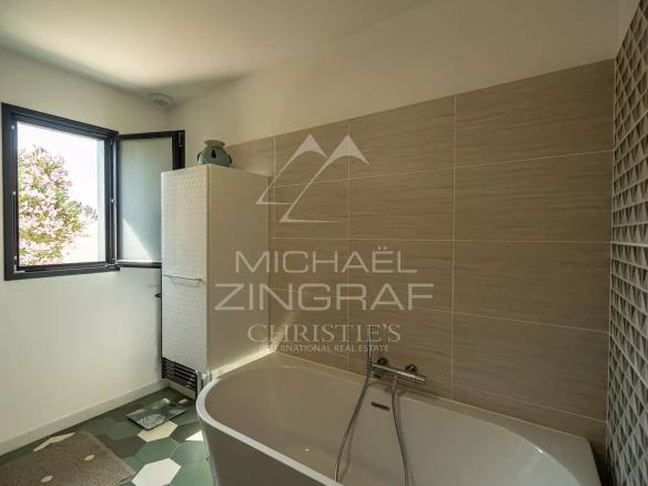 Modern bathroom with bathtub and open window, decorative tiling.