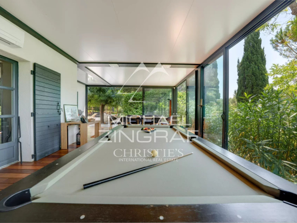 Interior of a property with a pool table, large bay windows and a view of the greenery.