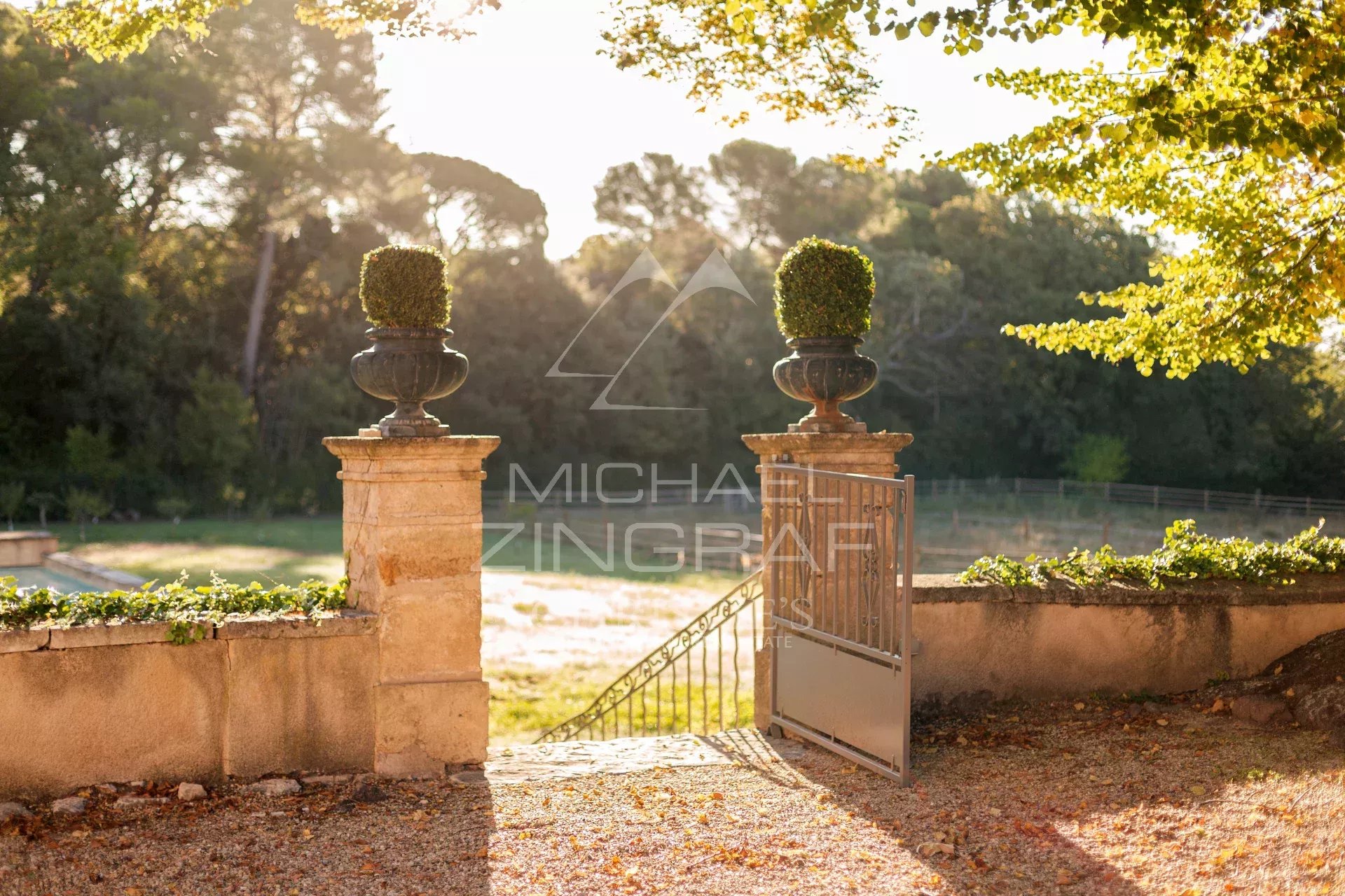 Entrée d’une propriété provençale Entrée d'une propriété avec des vases en pierre et un parc verdoyant en arrière-plan.