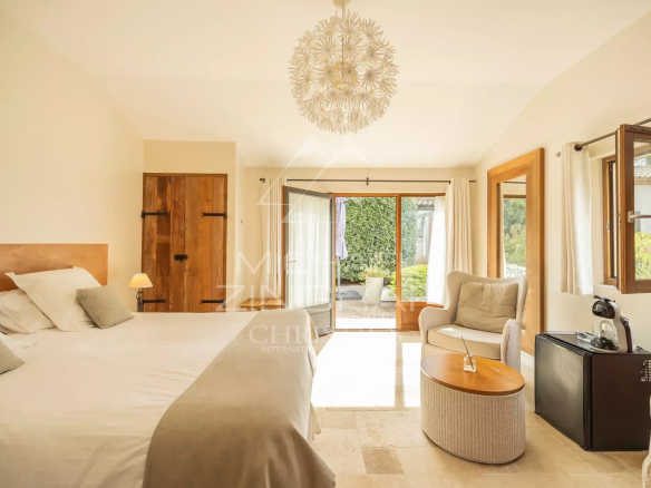 Chambre lumineuse avec lit double, fauteuil et accès à un espace extérieur.