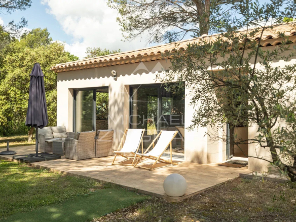 Terrasse d'une propriété rénovée avec chaises longues et parasol, entourée de verdure.