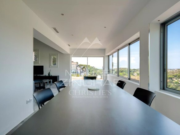 Intérieur d'une maison moderne avec vue sur la mer, grandes fenêtres et table à manger.