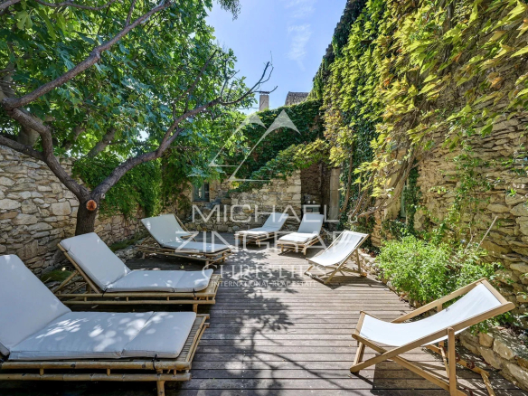 Wooden terrace with sun loungers and stone walls covered in greenery in a renovated property.