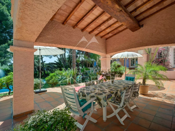 Terrace of a villa in La Ciotat with table and chairs, surrounded by greenery and parasols.
