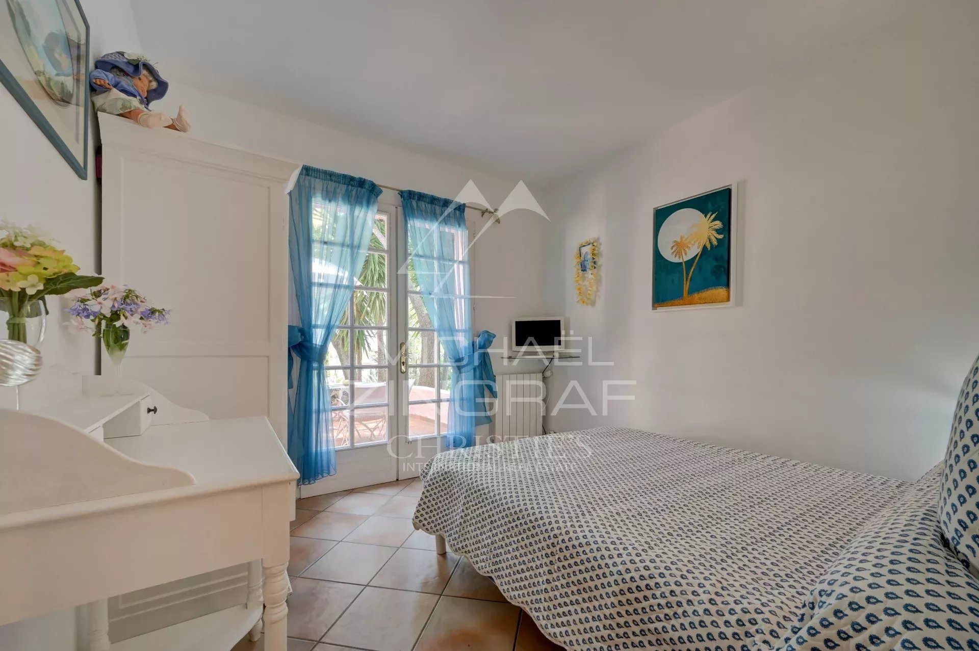 Room with a view Bright room with a single bed and windows draped with blue curtains.