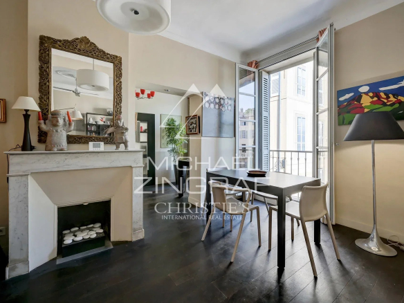 Intérieur d'un appartement ancien avec cheminée, table et fenêtres ouvertes sur la place des Prêcheurs à Aix-en-Provence.
