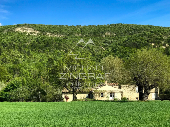 A renovated 17th-century mill surrounded by greenery in Forcalquier, with the Lure mountain in the background.
