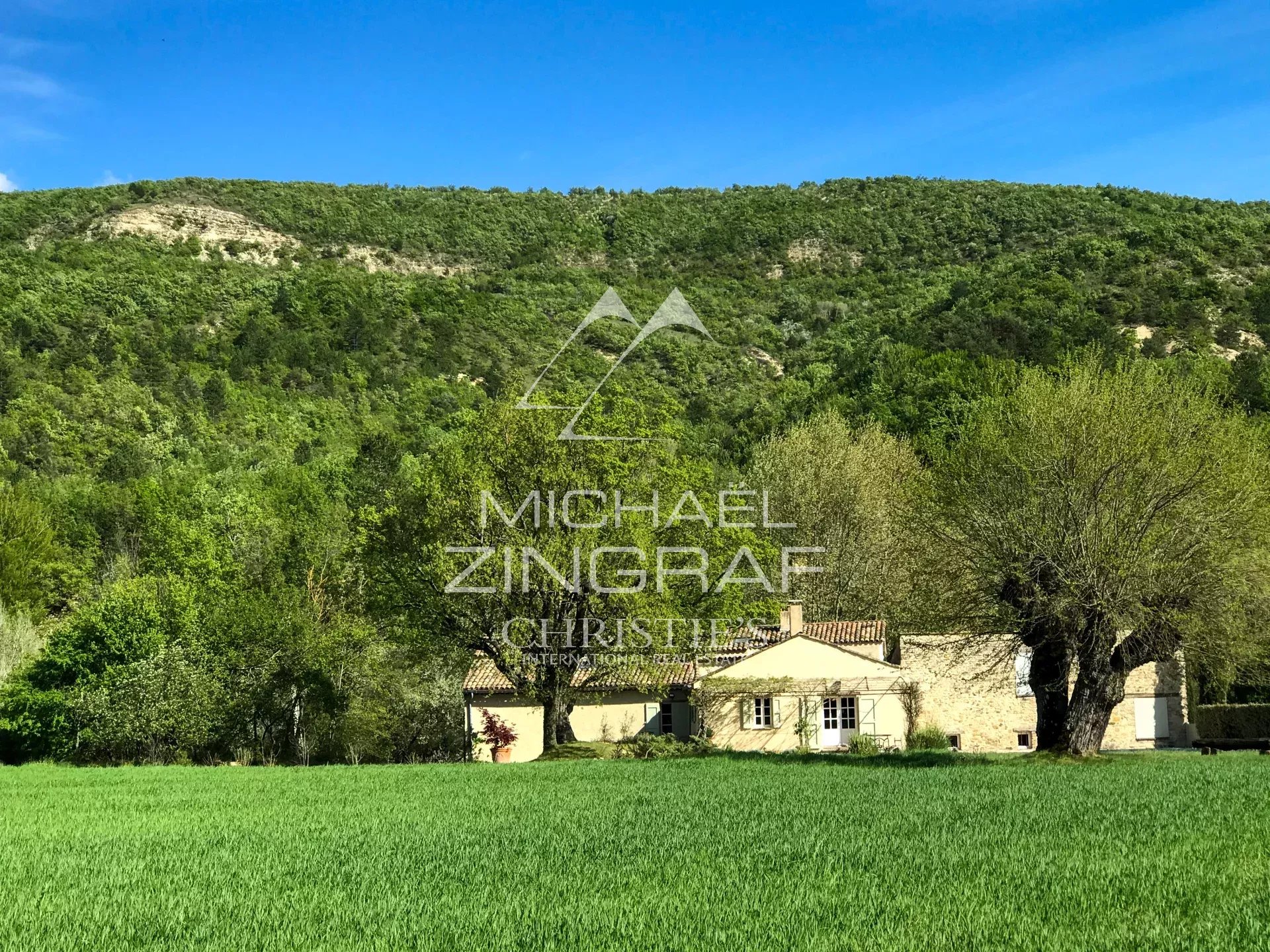 Renovated 17th-century mill in Forcalquier A renovated 17th-century mill surrounded by greenery in Forcalquier, with the Lure mountain in the background.