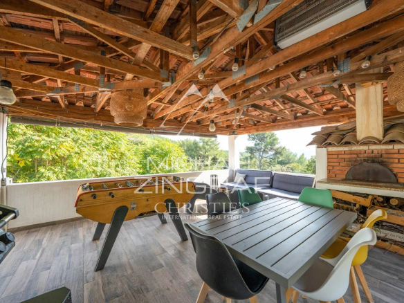 Terrasse couverte avec mobilier de jardin et barbecue dans une maison en pleine colline.