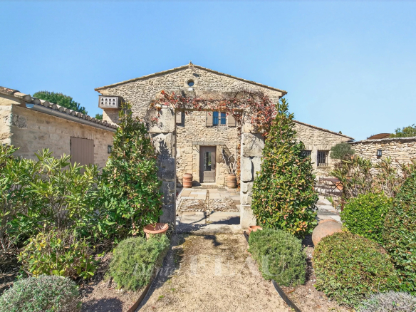 Rustic stone house with a cobblestone path and lush greenery in a sunny courtyard.