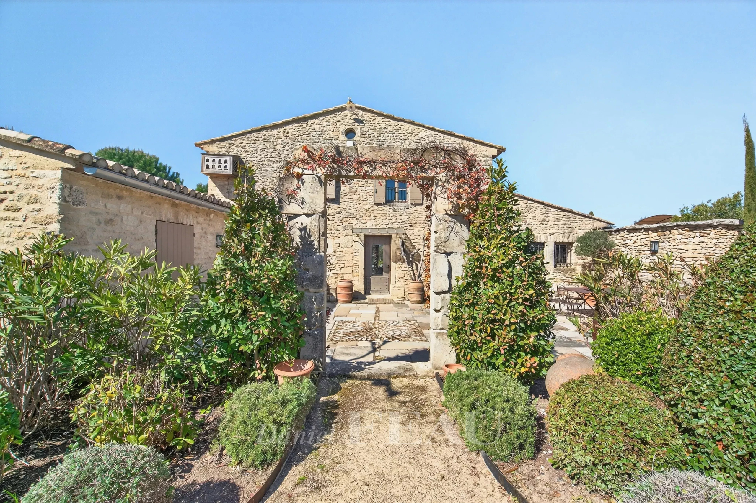 Rustic stone house with a cobblestone path and lush greenery in a sunny courtyard.