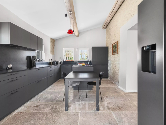Modern grey kitchen with dark cabinets, stone wall, and a central island with two chairs under wooden ceiling beams.