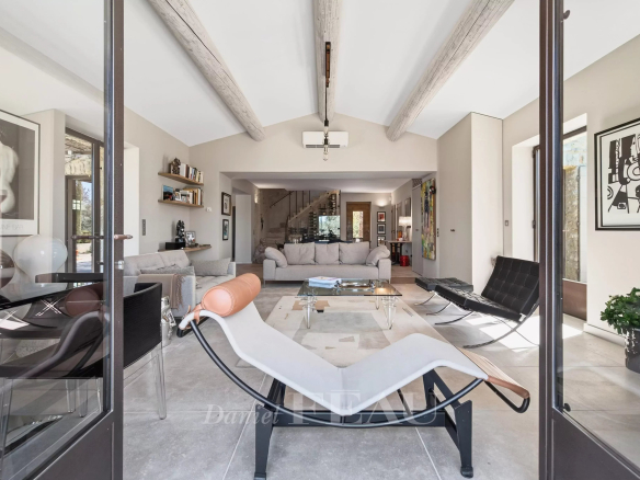 Open-plan living room viewed through glass doors, foregrounded by a white chaise lounge and modern seating area.