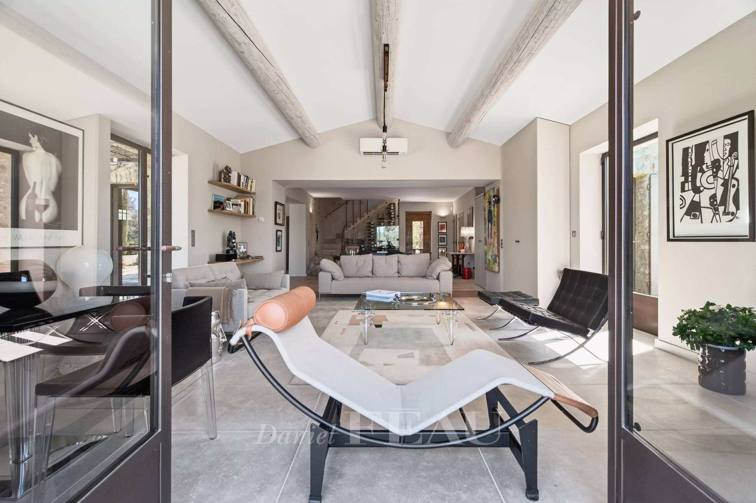 Open-plan living room viewed through glass doors, foregrounded by a white chaise lounge and modern seating area.