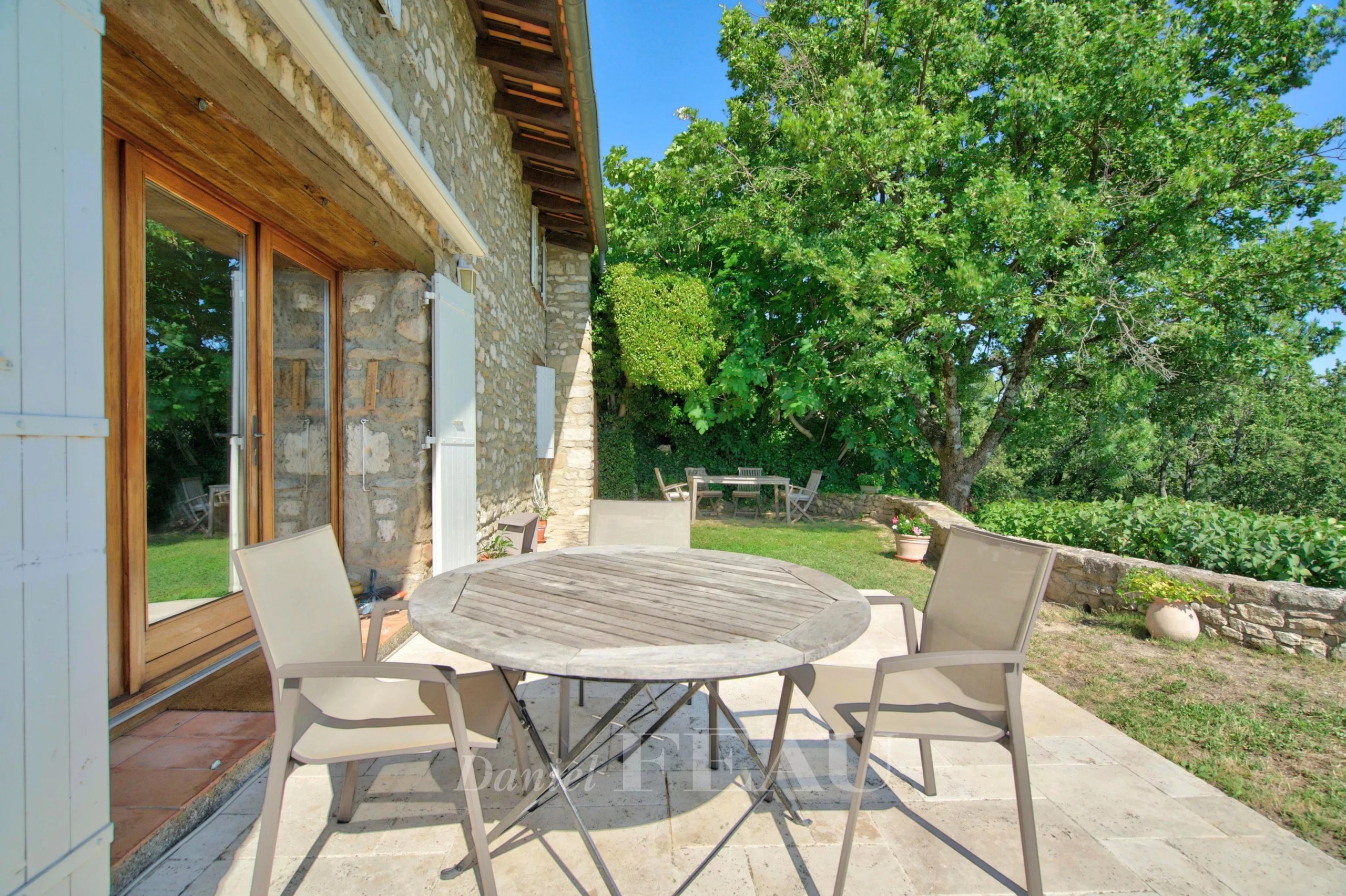 Stone terrace with round table and chairs, overlooking the green countryside in Montjustin.