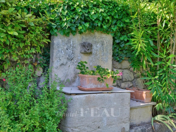 Stone fountain surrounded by greenery with flower pots in Montjustin.
