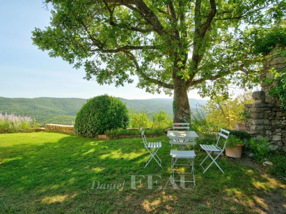 Terrace with table and chairs under a tree, overlooking the valley at Montjustin.