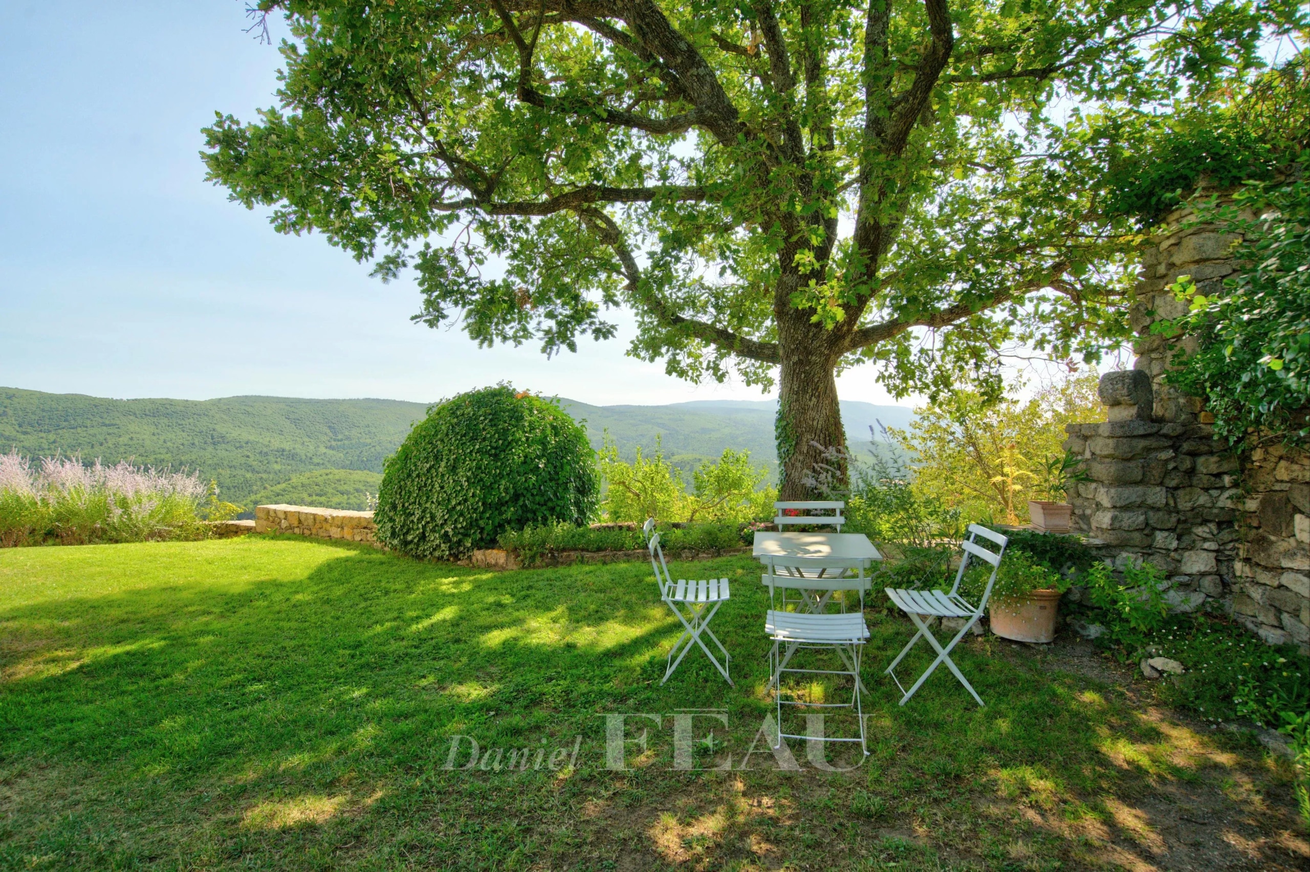 Terrace with table and chairs under a tree, overlooking the valley at Montjustin.