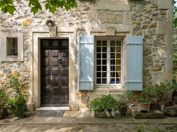 Entrée d'un mas en pierre avec porte en bois et fenêtres à volets bleus, entouré de verdure.