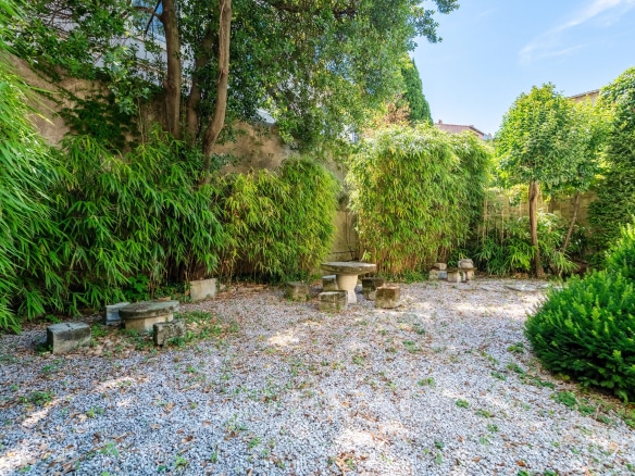 Jardin arboré d'un hôtel particulier du XIXème siècle à Avignon, avec des pierres et des plantes.