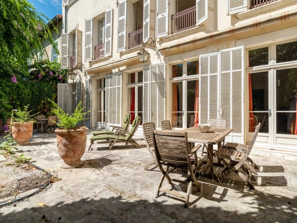 Terrace of a 19th century private mansion in Avignon with wooden furniture and green garden.