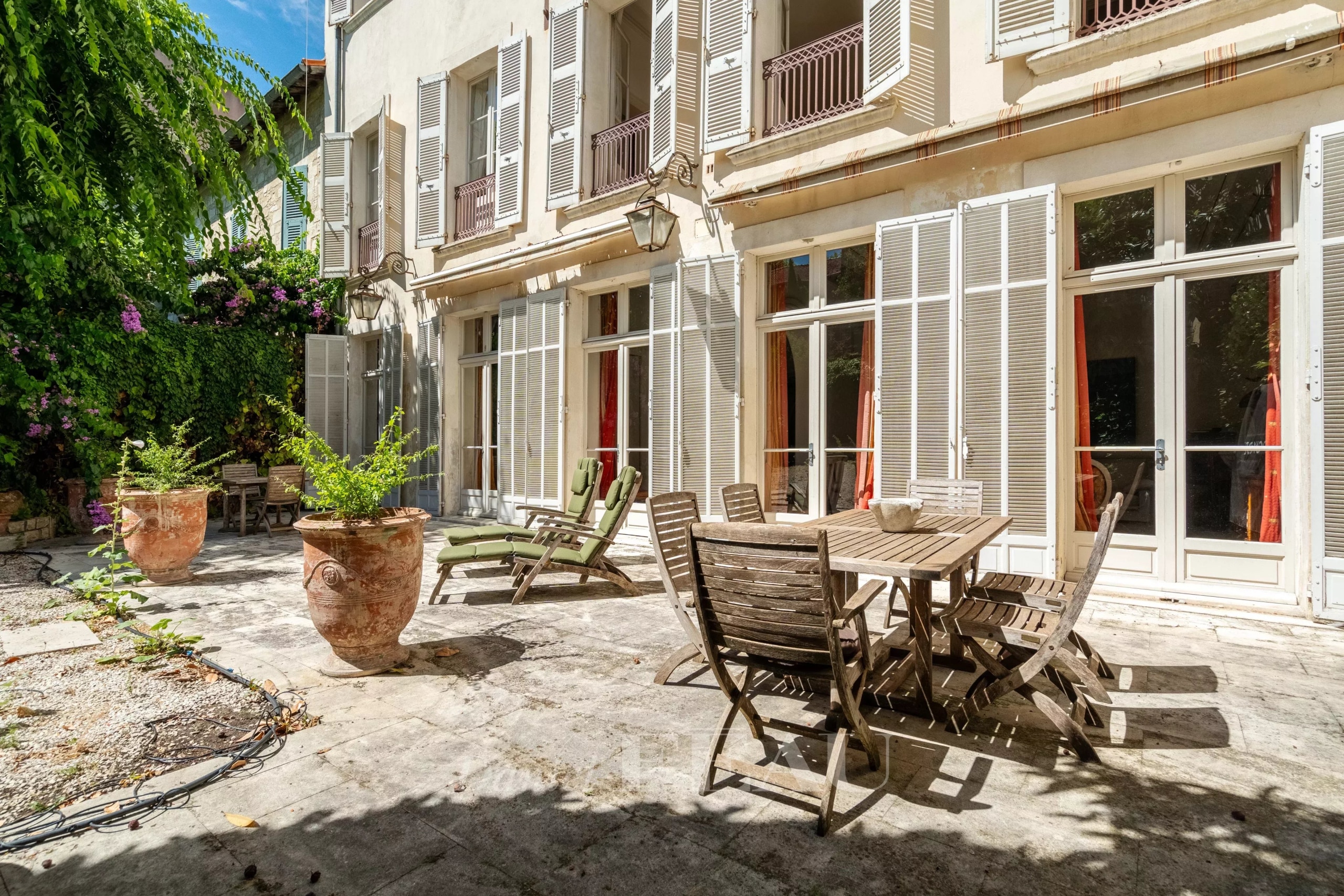 Terrasse d'un hôtel particulier du XIXème siècle à Avignon avec mobilier en bois et jardin verdoyant.