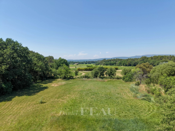 Vue dégagée sur un parc verdoyant avec des arbres et des collines en arrière-plan à Ménerbes.