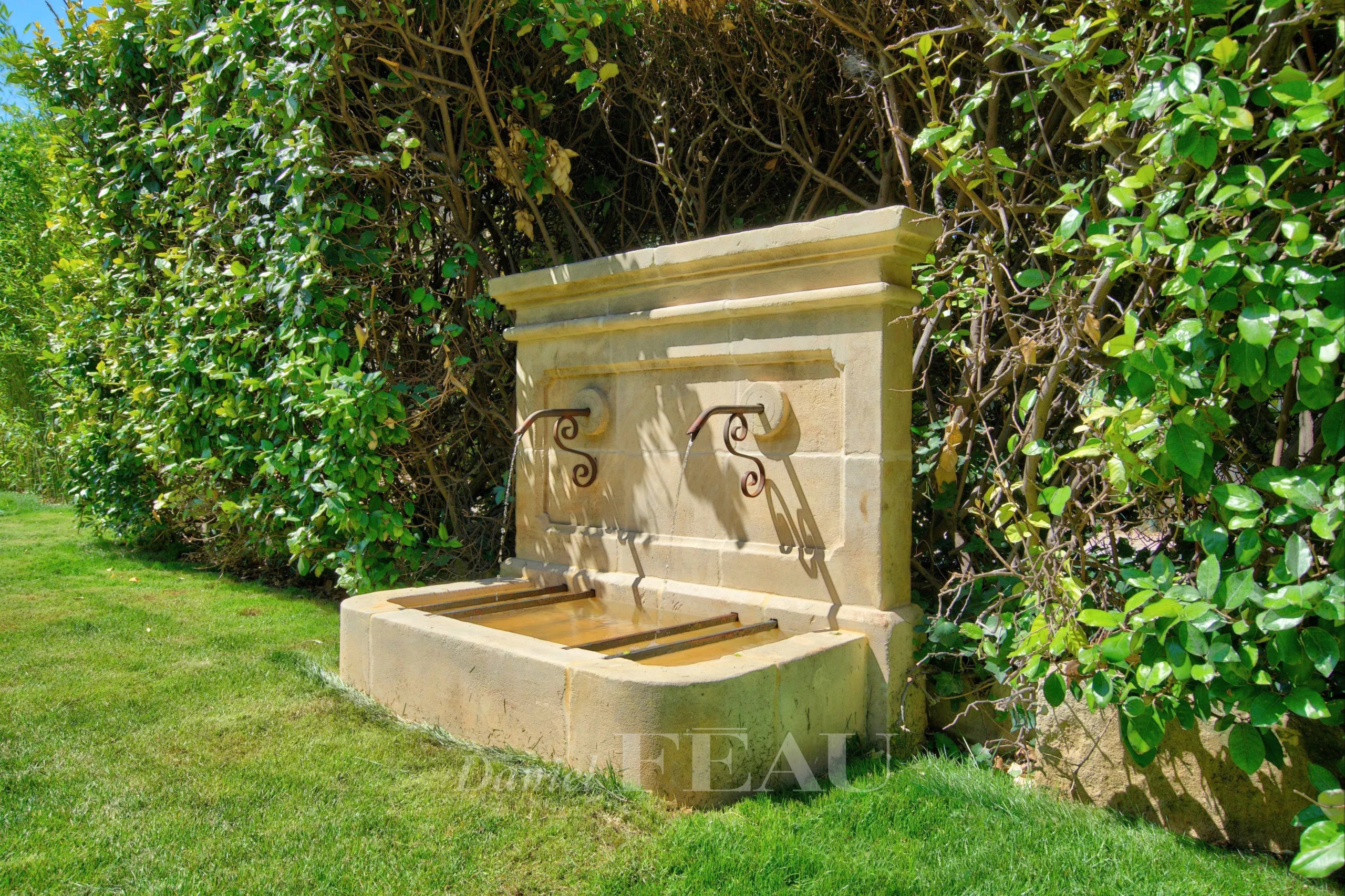 Fontaine en pierre dans un jardin paysager avec des plantes méditerranéennes
