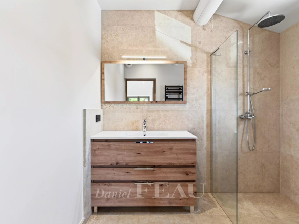 Salle de bain moderne avec douche et meuble en bois, murs en pierre beige.
