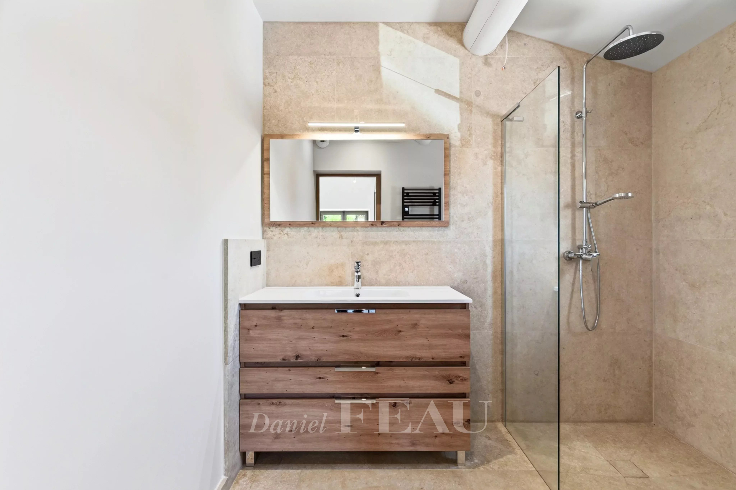 Salle de bain moderne avec douche et meuble en bois, murs en pierre beige.
