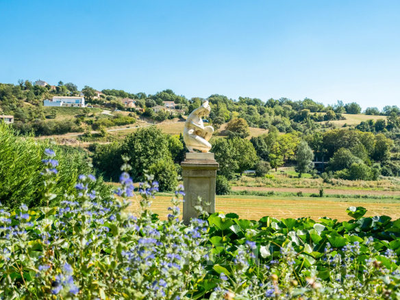 Vue d'un paysage avec une sculpture sur un socle, entourée de fleurs et de verdure à Valensole.